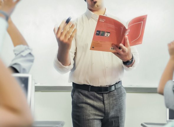 Male teacher standing before students (8-10) with hands raised